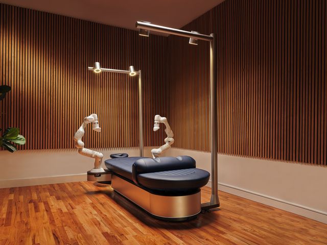 An empty Aescape machine massage table in a room with wood floors and panel walls.