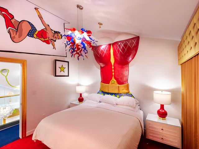 The Wonder Woman room at The Roxbury with a mural of Wonder Woman, a bust of her uniform above the bed, and gold accents.