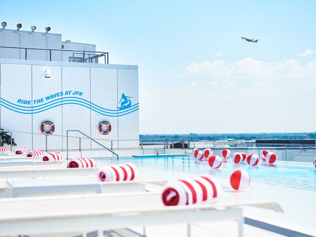 A pool with red and white balls on the water and red and white towels on the white chairs with a plane in the sky.