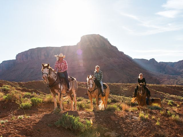 People riding horses next to red rock formations in Utah.
