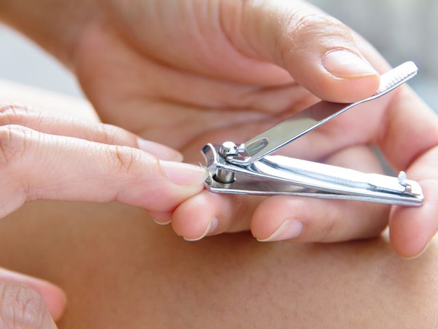 Manicured hands are seen using silver nail clippers to trim nails.