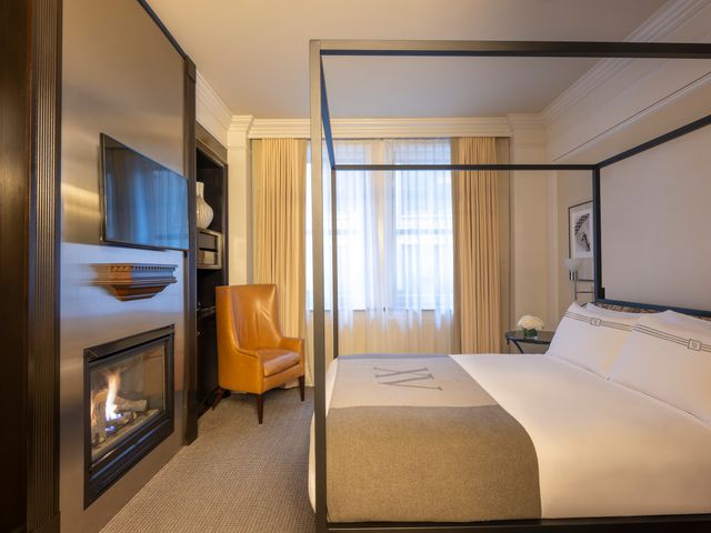 A hotel guest room with a canopy bed and a TV above a fireplace.