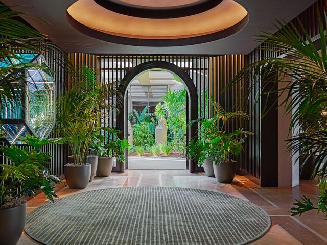 A lush entryway filled with green leafy plants and statement slotted walls and archways.