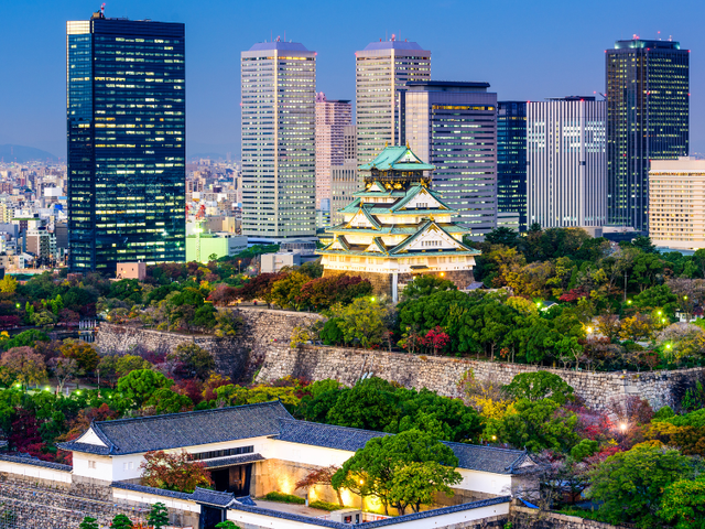 The skyline of Osaka, Japan, with tall buildings in the background and a temple in the middle.