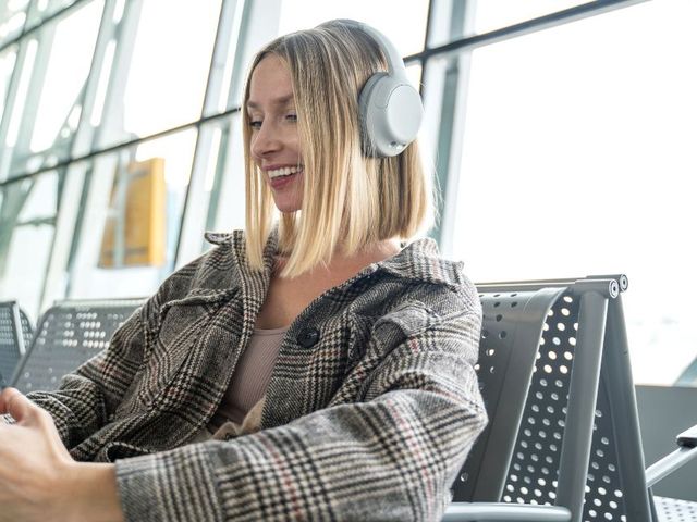 A woman sits in an airport holding her phone with headphones on.