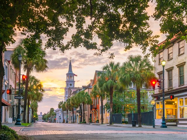 A road of colorful homes lined with palm trees with the sun setting in the background.