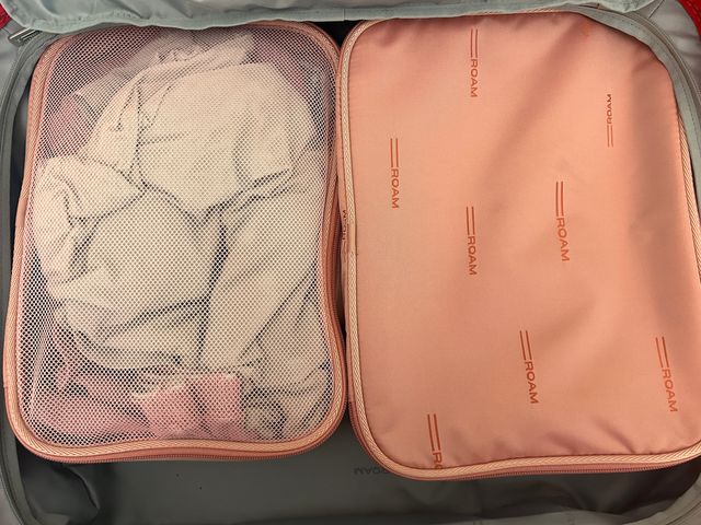 Two peach colored packing cubes inside a suitcase with one seen with a matte logo side and the other with a mesh cover.