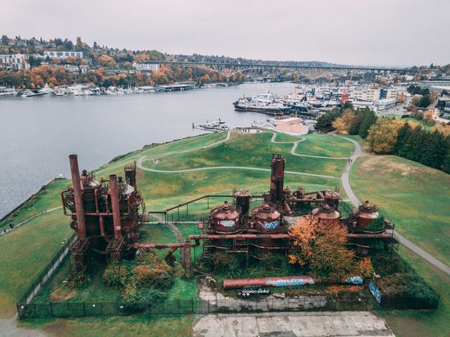 An aerial view over Gas Works Park in Seattle with industrial buildings on a large green lawn next to the water.