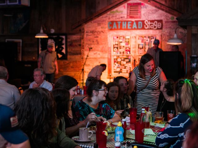 A crowded restaurant with people congregating at a table in front of a stage.