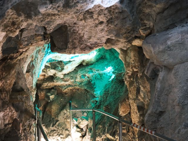 A lit-up railing leads down into a rocky cave.