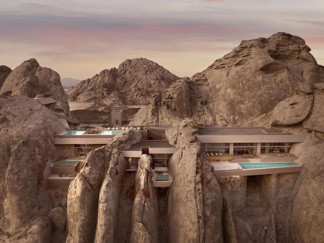 A mountain rock wall covered with cliffside cave rooms with pools.