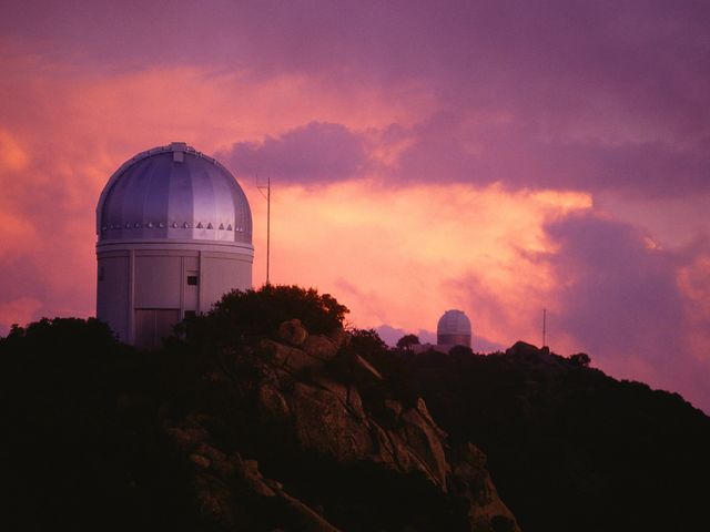 The dome of an observatory as seen at sunset on a hill.