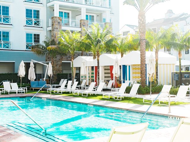A hotel pool surrounded by white lounge chairs, colorful cabanas, and palm trees.