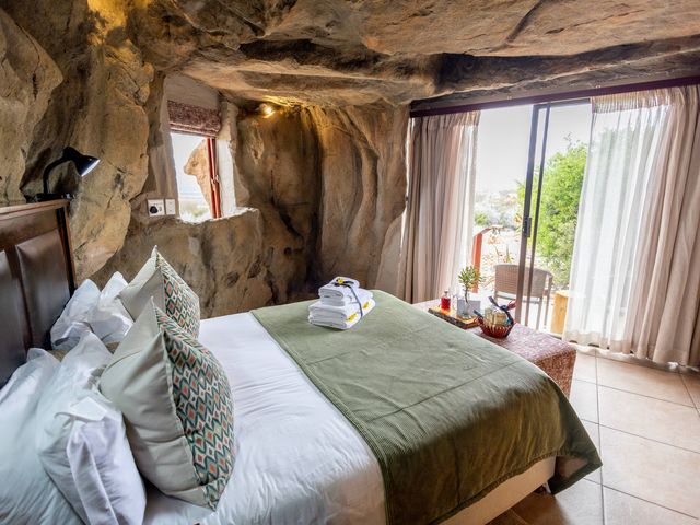 Inside a cave room at Kagga Kamma Eco Lodge with a bed and a bench facing patio doors.