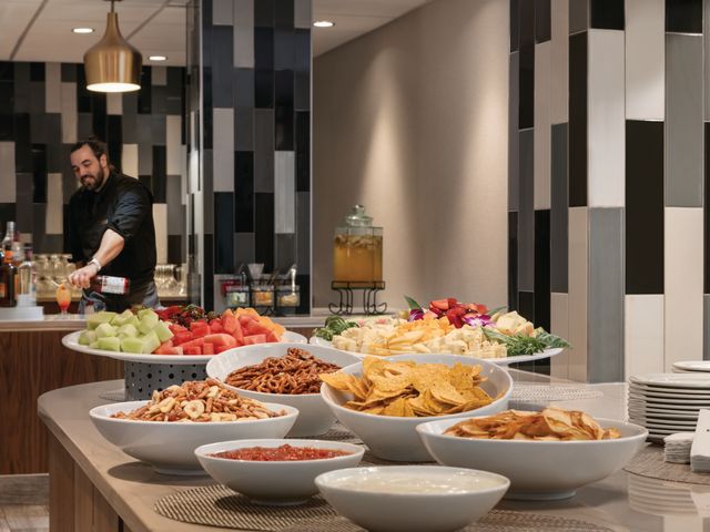 A table filled with white bowls full of fruit, chips, pretzels, dips, and more.