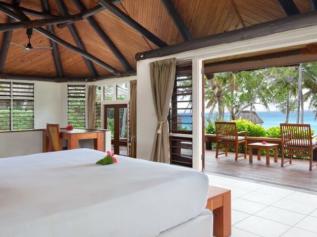 A guest room at Yasawa Island Resort with a large bed facing to open terrace doors facing the ocean.