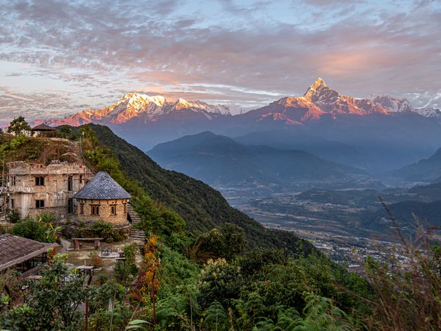 Sunrise on the Himalayas in Nepal with an old building in the foreground.