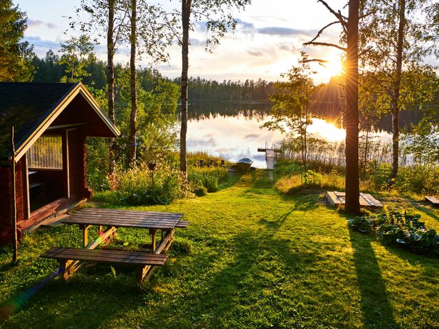A small cabin with a picnic table overlooking a body of water through the trees at sunset.