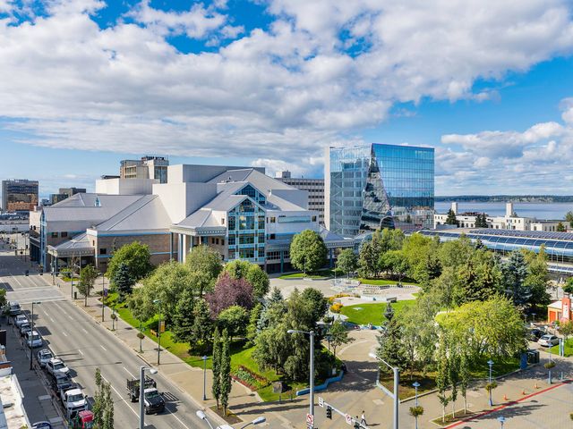 A modern looking building in downtown Anchorage next to water and a parking lot full of cars. 