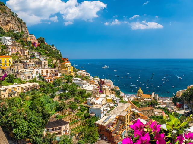 Hillsides dotted with buildings and trees and flowers with views of the water along the Amalfi Coast.