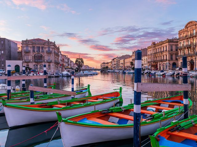 A waterfront area in Sète, France, with colorful canoes in front, and buildings on either side of the water.