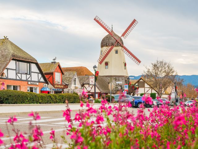 A street with a windmill and Danish architecture framed by pink flowers in Solvang.