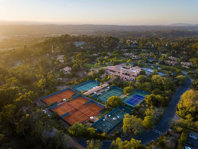 An overhead drone shot taken at sunset of the clay tennis courts at Rancho Valencia Resort & Spa in San Diego.