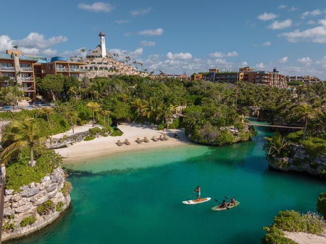 A view of a beach with turquoise waters and paddleboarders next to a lush coastline at Hotel Xcaret in Mexico.