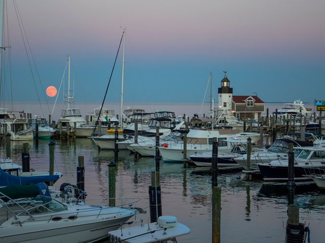 A marina filled with boats in the water with a low pink moon.
