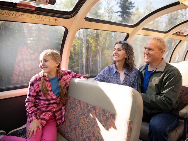 A family of three sitting and smiling in a domed car on the Alaska Railroad.