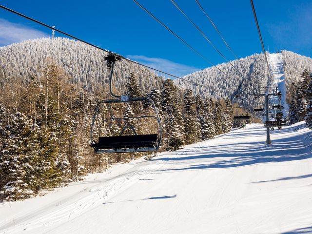 A chair lift surrounded by snowy terrain and snow-capped trees and mountains at Angel Fire Resort in New Mexico.