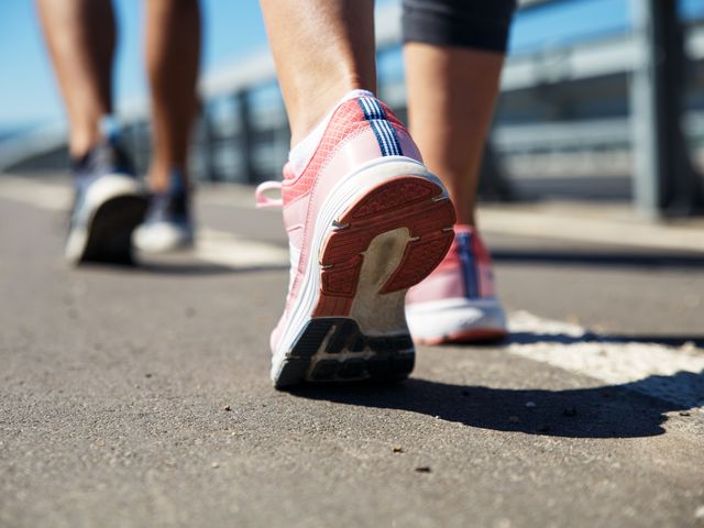 A pink pair of sneakers in motion while walking down a road.
