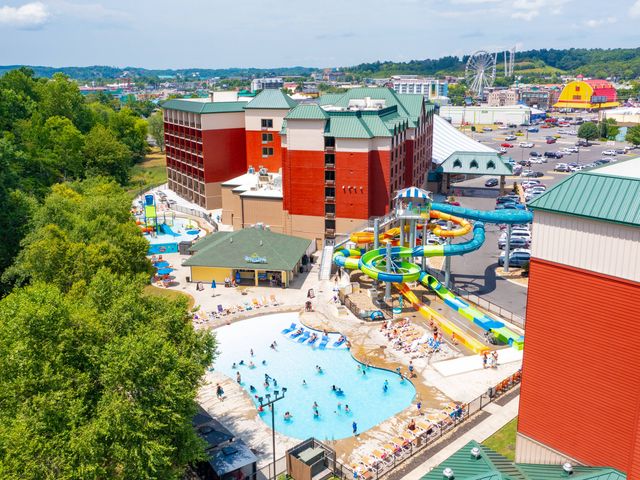 A hotel seen from outside with a pool deck that has a zero-entry pool and water slides, and an amusement park in the distance.