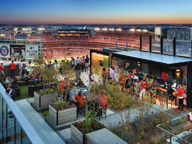 A hotel rooftop filled with people watching a baseball game at the stadium next door.