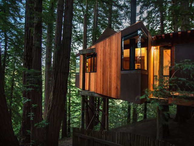 A woodsy-looking treehouse with the lights on inside surrounded by trees at Post Ranch Inn.