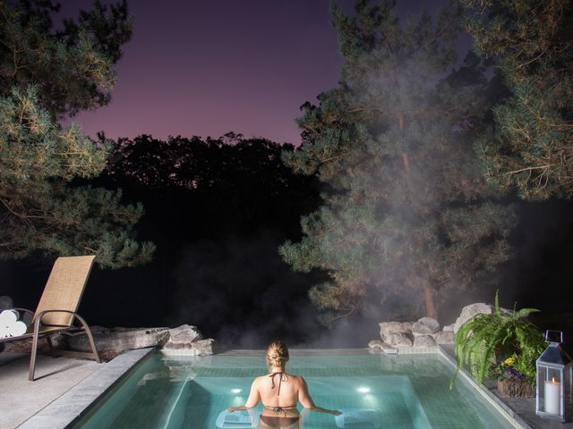 A woman is seen from behind in a hot tub at night as steam rises above.