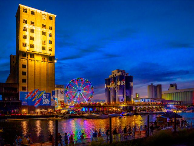  View of Buffalo's RiverWorks entertainment district at night, with a blue sky, lit-up ferris wheel, and the glistening Buffalo River.
