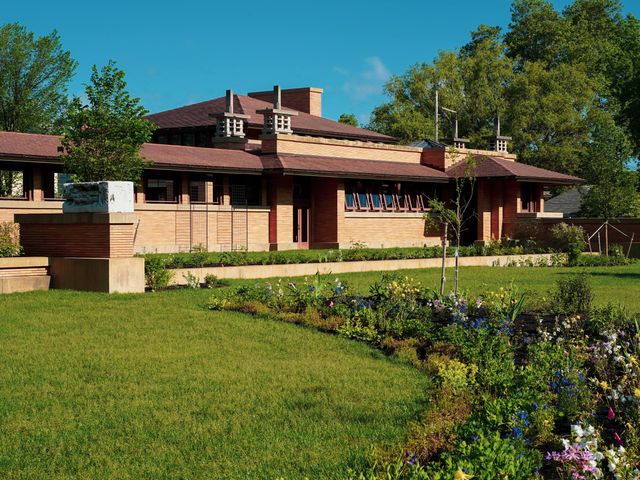 Daytime exterior of Frank Lloyd Wright's famous Buffalo residence, The Martin House, with green trees in the background and lawn in front