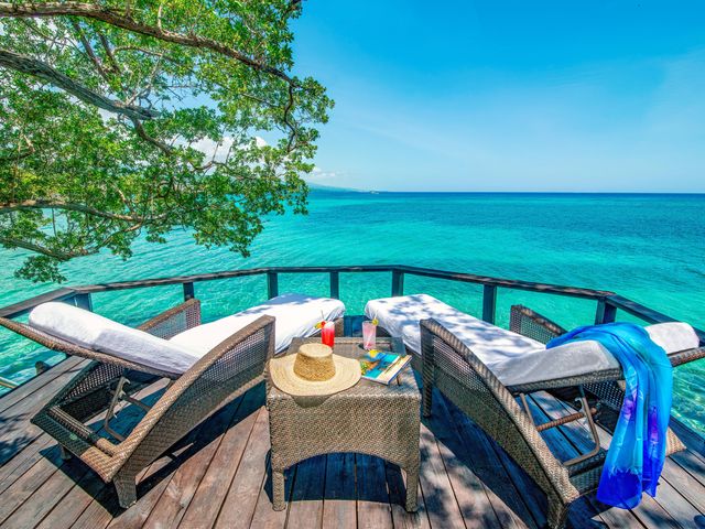 Two lounge chairs on a deck with an ottoman in between facing the turquoise blue water at Jamaica Inn Resort Hotel.