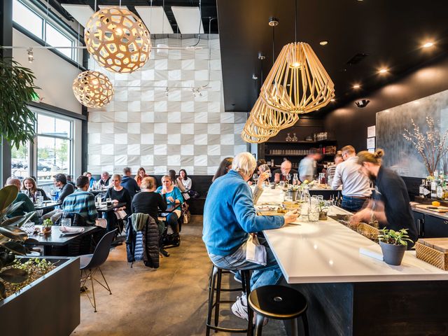 People sitting at tables and at the bar inside a modern looking restaurant with large pendant lantern lights.