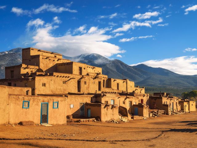 A grouping of adobe buildings in Taos Pueblo with distant mountain views.
