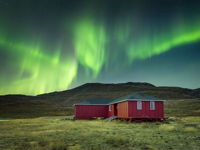 Green northern lights shining over a red wooden cottage in Kangerlussuaq, Greenland.