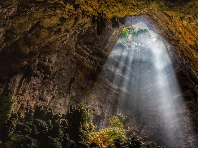 Inside a cave in Italy with a circular hole on top and light streaming through.