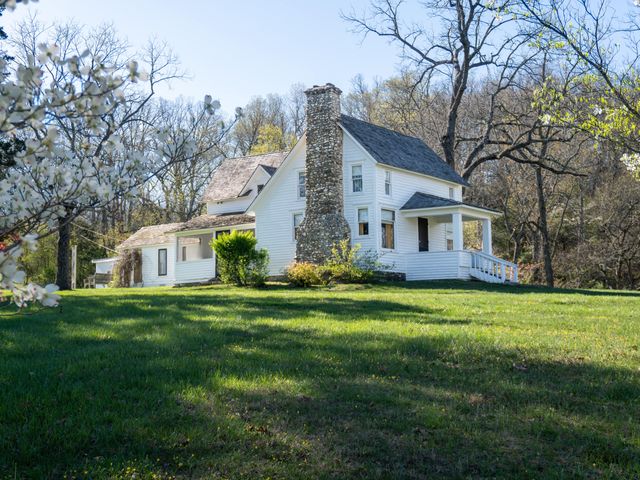 The white exterior of the Laura Ingalls Wilder Historic Home and Museum where author lived and wrote books were written, on a grassy lawn.