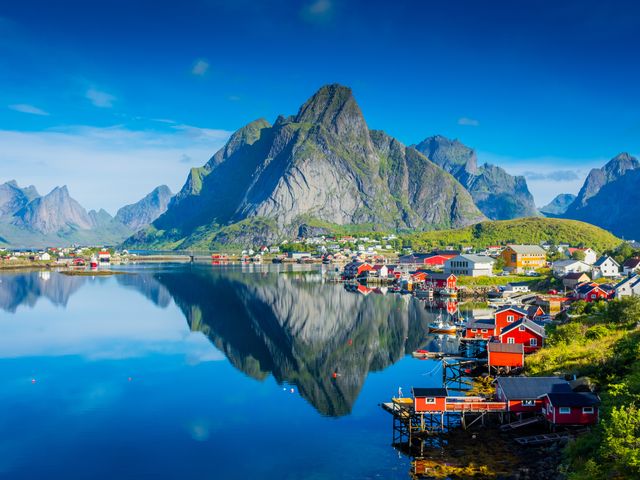 A village of colorful houses facing the water with a reflection of the mountains in Norway's Lofoten Islands.