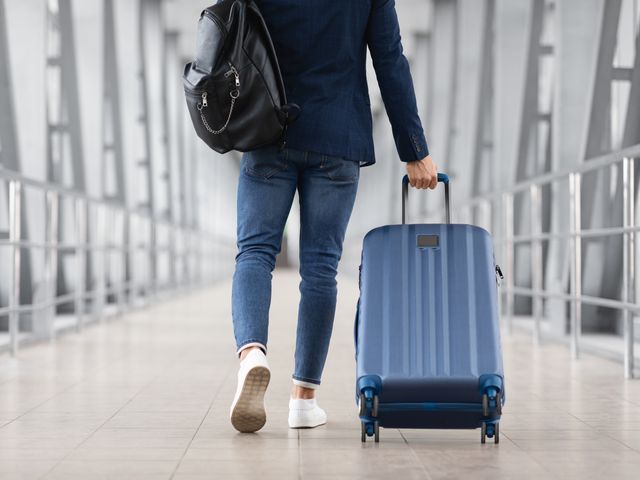 A man rolls a suitcase through an airport while carrying a backpack.