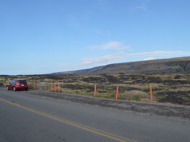 A red car parked on the side of a road next to lava field at Hawaiʻi Volcanoes National Park.