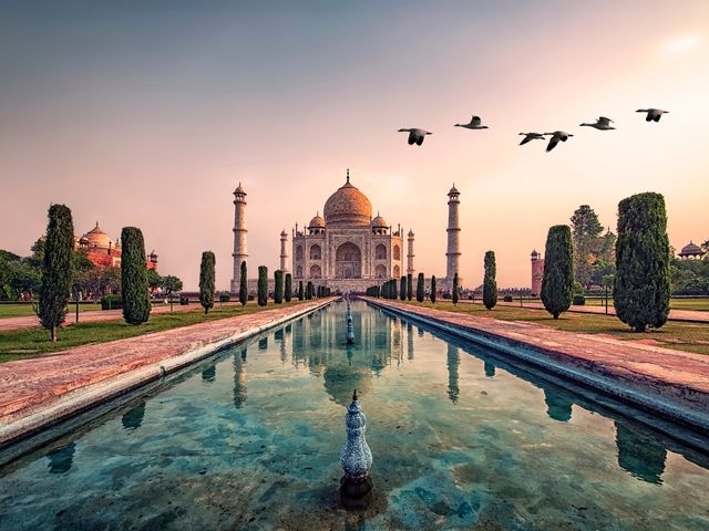 The Taj Mahal Palace in India as seen from one end of a reflecting pool at dusk.