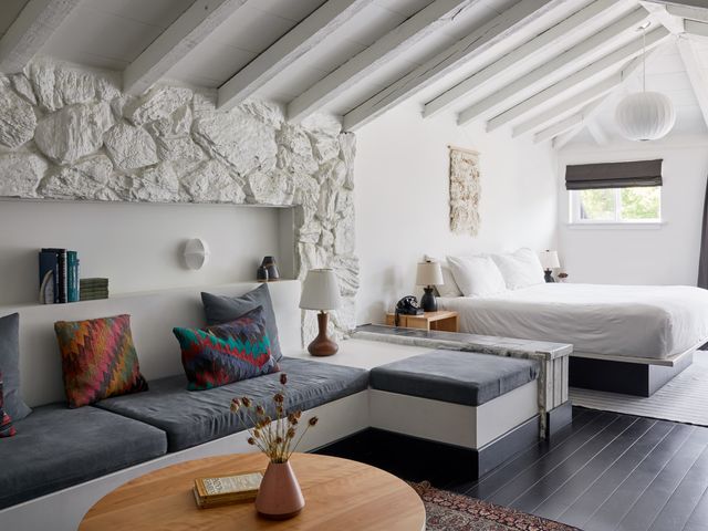 A hotel room with beamed ceilings, white walls, a large bed, and a separate seating nook area.