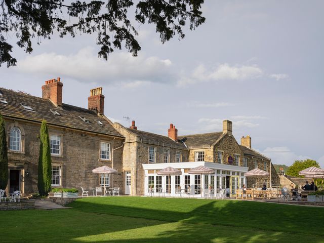 The exterior of The Cavendish Hotel with lots of white chairs and striped umbrellas next to a green lawn.